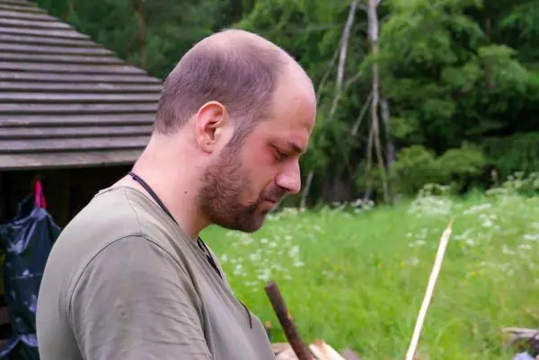 Mann steht in der Natur und betrachtet Holzstücke