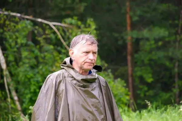 Mann trägt einen grünen Regenponcho in einer bewaldeten Umgebung