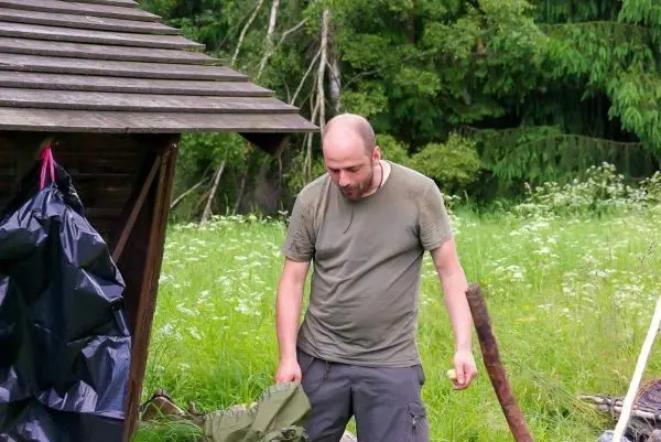 Mann überprüft Ausrüstung neben einer Holzstruktur in einer grünen Wiese