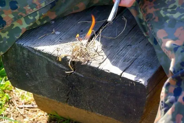 Person entzündet trockenes Gras auf einem Holzblock