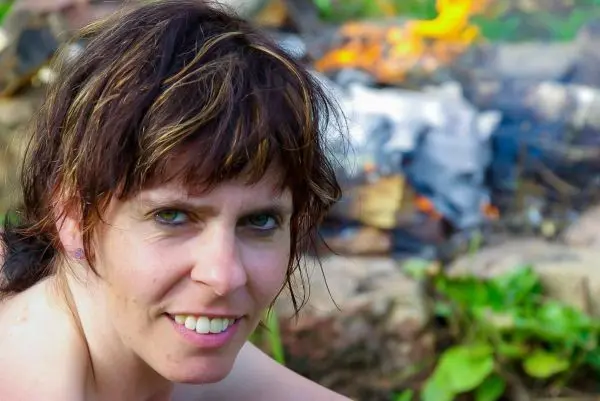Person sitzt lächelnd vor einem Feuer
