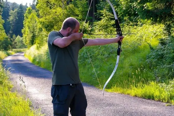Person spannt einen Bogen auf einem Weg zwischen Bäumen