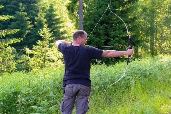 Person spannt einen Bogen in einer bewaldeten Umgebung