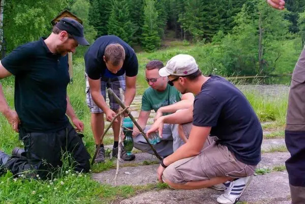 Vier Personen knien um eine selbstgebaute Konstruktion aus Ästen und einem Glas