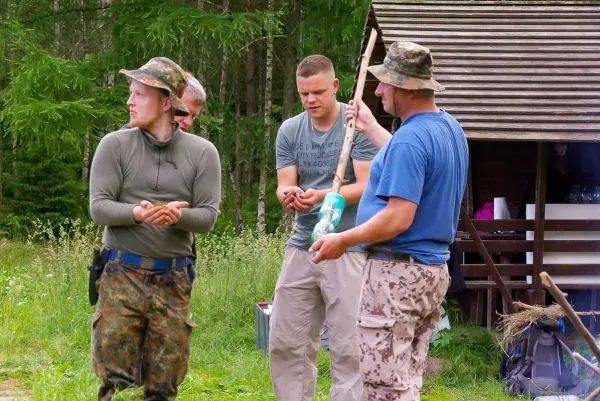 Vier Personen stehen in einer Wiese und halten verschiedene Gegenstände in den Händen
