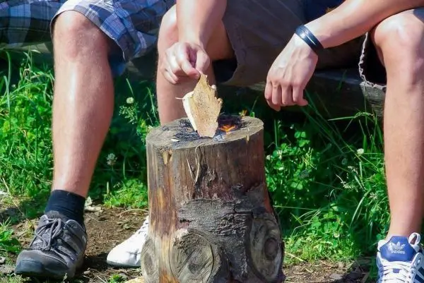 Zunder glimmt auf einem Holzstamm, während eine Hand ihn hält