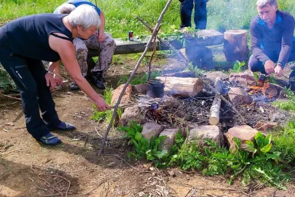 Zunder glimmt in einem kleinen Bodenfeuer, während jemand mit einem Stock hantiert