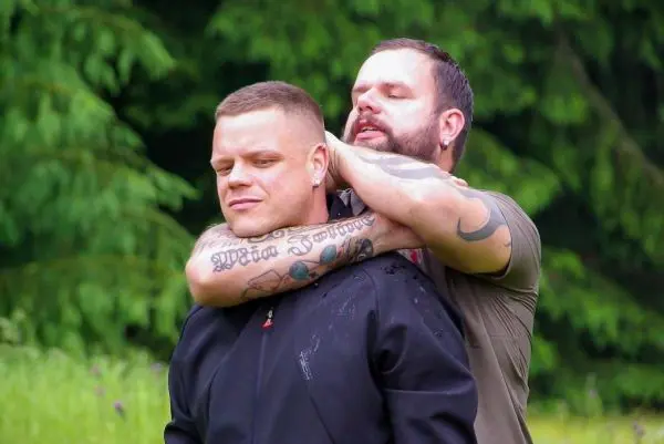 Zwei Männer in einem Wald, einer hält den anderen von hinten fest