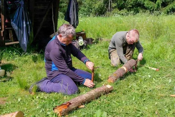 Zwei Personen bearbeiten Holzstücke mit Messern auf einer Wiese