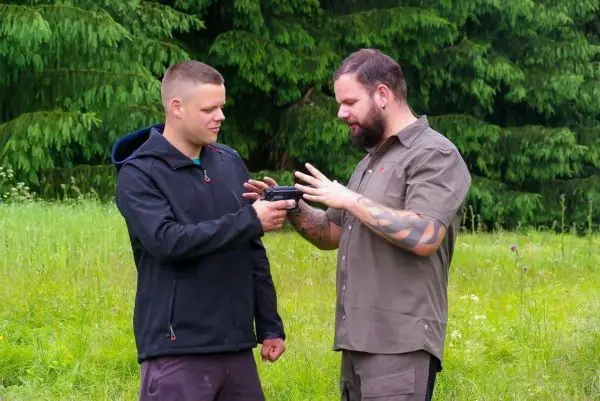 Zwei Personen halten eine Handfeuerwaffe in einem grünen Feld