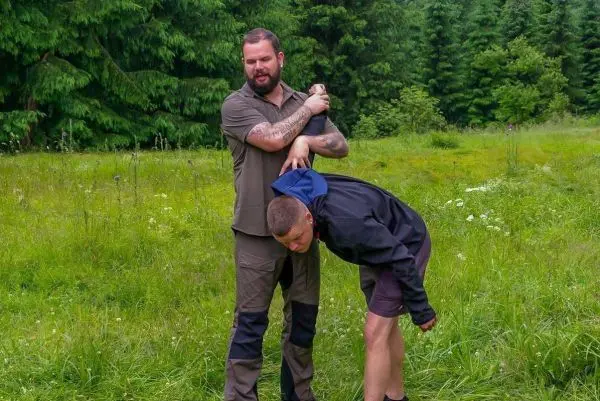 Zwei Personen in einem grünen Feld, eine Person hält die andere in einer kontrollierenden Position
