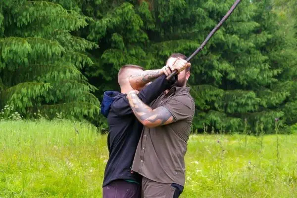 Zwei Personen kämpfen um die Kontrolle über einen langen Stock in einer grünen Wiese