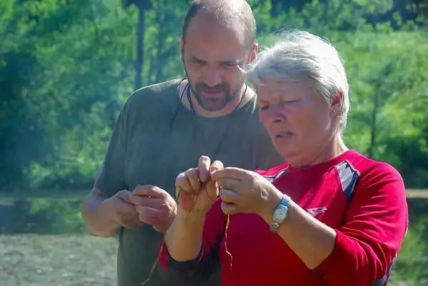 Zwei Personen knoten Schnüre am Ufer eines Gewässers