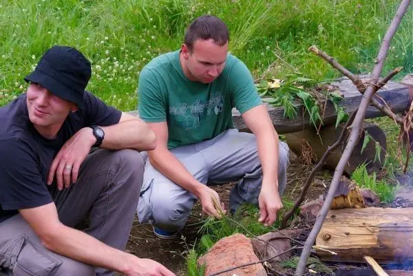 Zwei Personen sitzen am Boden und bereiten etwas über dem Feuer vor beim Survival Training