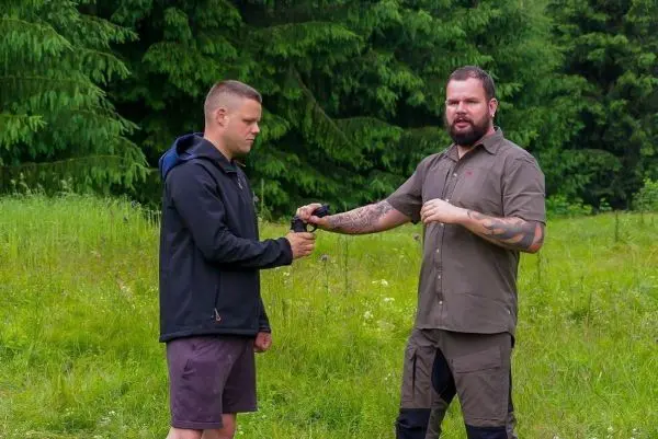 Zwei Personen stehen in einer Wiese und führen eine Übergabe durch