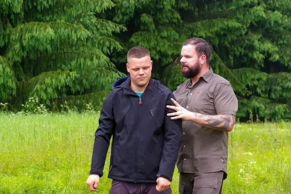 Zwei Personen stehen in einer Wiese und sprechen miteinander