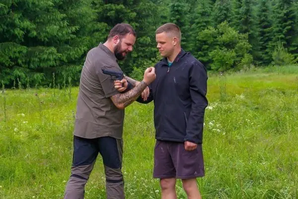 Zwei Personen üben eine Selbstverteidigungstechnik im Freien mit einer Handfeuerwaffe