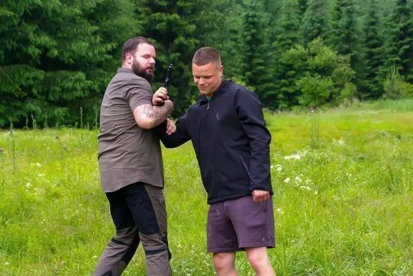 Zwei Personen üben eine Selbstverteidigungstechnik im Freien mit einer Waffe
