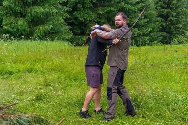 Zwei Personen üben eine Selbstverteidigungstechnik mit einem Stock im Gras