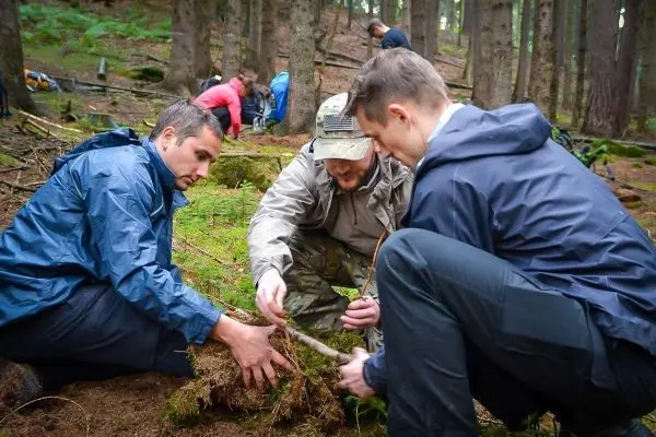 Drei Personen arbeiten am Boden und formen eine Konstruktion aus Ästen