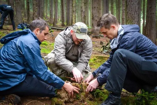 Drei Personen arbeiten gemeinsam am Boden im Wald, um Materialien zu sammeln
