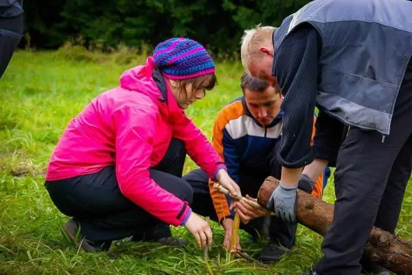 Drei Personen arbeiten gemeinsam an einem Holzstück im Gras