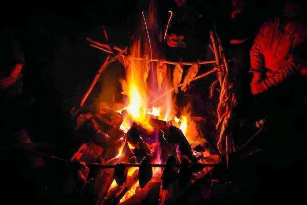 Feuer brennt zwischen Holzstöcken, umgeben von Personen