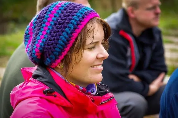 Frau mit buntem Hut und roter Jacke sitzt lächelnd in einer Gruppe