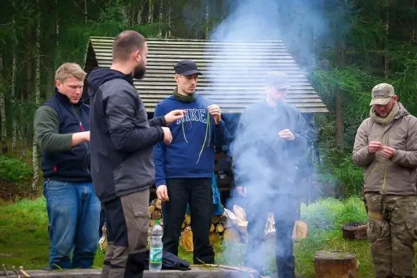 Fünf Personen halten Schnüre und stehen um einen rauchenden Feuerplatz