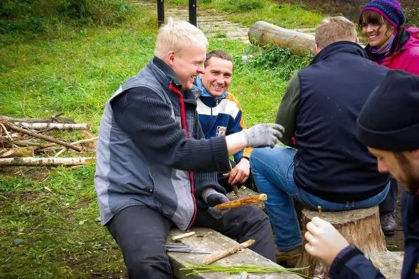Gruppe arbeitet an Holzstücken auf Baumstämmen im Freien