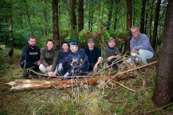 Gruppe sitzt im Wald auf dem Boden, umgeben von Bäumen und Ästen