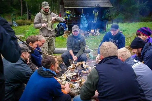 Gruppe sitzt um ein Feuer und röstet Stockbrot über den Flammen