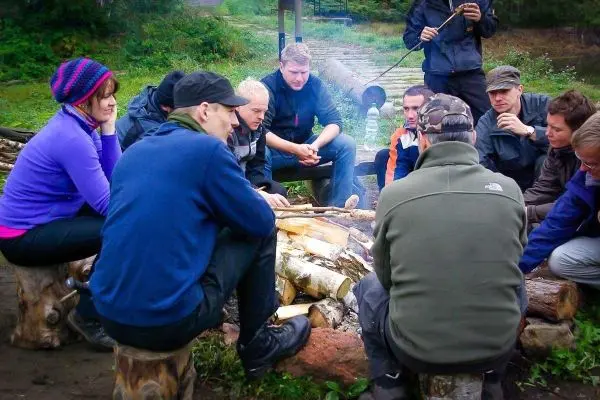 Gruppe sitzt um ein kleines Feuer und diskutiert Holzarbeiten