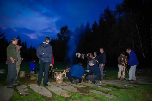Gruppe um ein Feuer, Fisch wird über dem offenen Feuer gegart