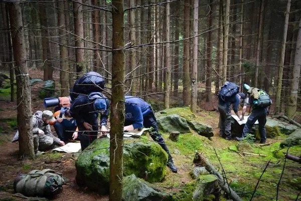 Gruppe von Personen studiert Karten auf Steinen im Wald beim Überlebenstraining
