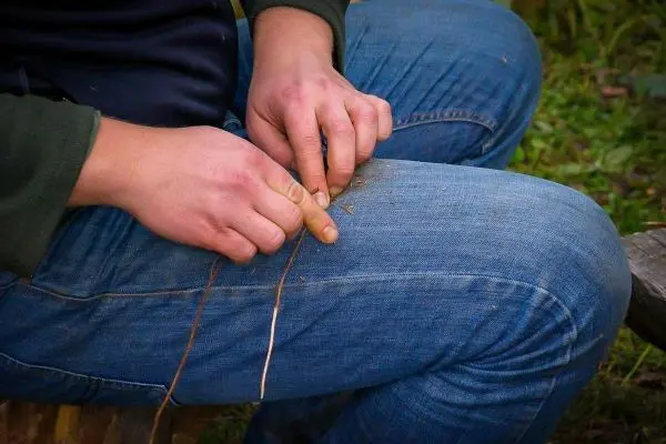Hände flechten dünne Pflanzenfasern auf den Oberschenkeln