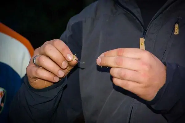 Hände halten einen kleinen Haken und eine Schnur zum Angeln