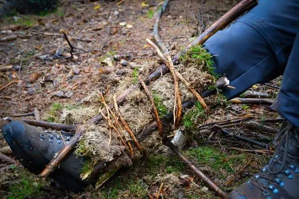 Improvisierte Schiene aus Ästen und Moos zur Stabilisierung eines Beins