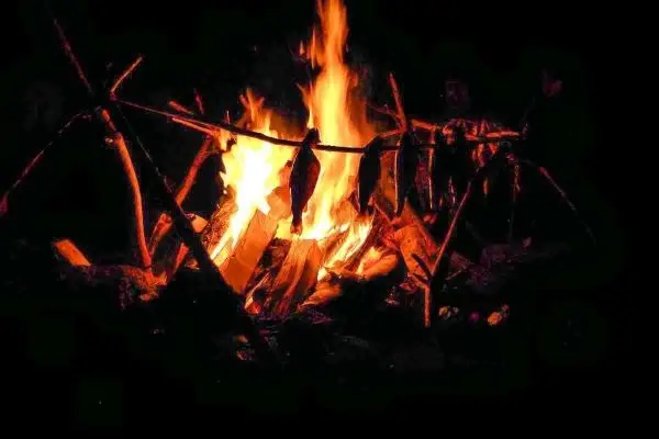 Kleine Flamme brennt unter einem Holzgestell mit Fisch