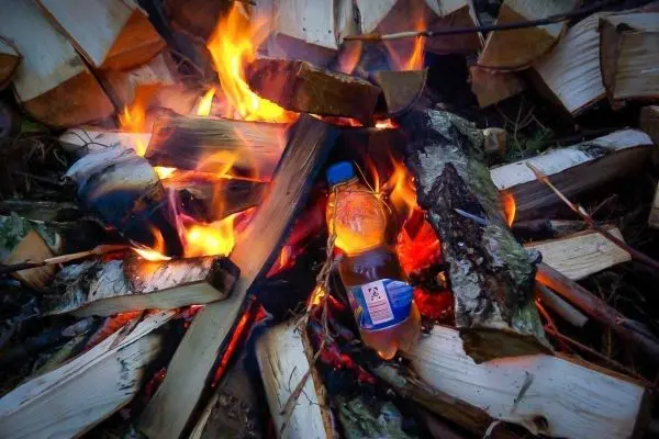 Kleine Flamme umgibt eine Wasserflasche zwischen Holzscheiten