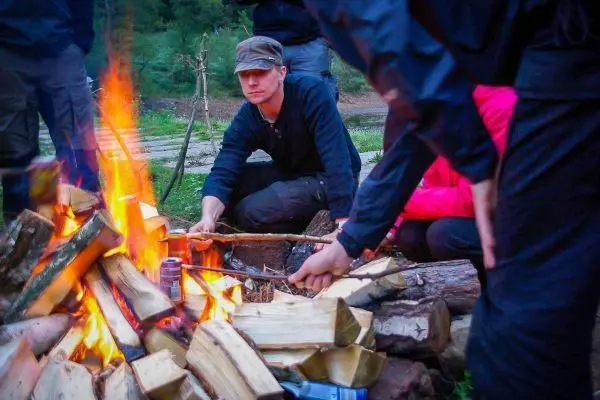 Kleines Bodenfeuer mit Holzscheiten, Person rührt mit Stock im Feuer