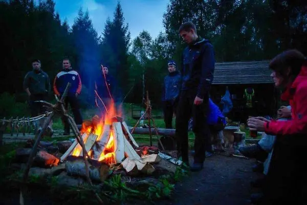 Kleines Bodenfeuer mit Holzscheiten, umgeben von mehreren Personen in der Dämmerung