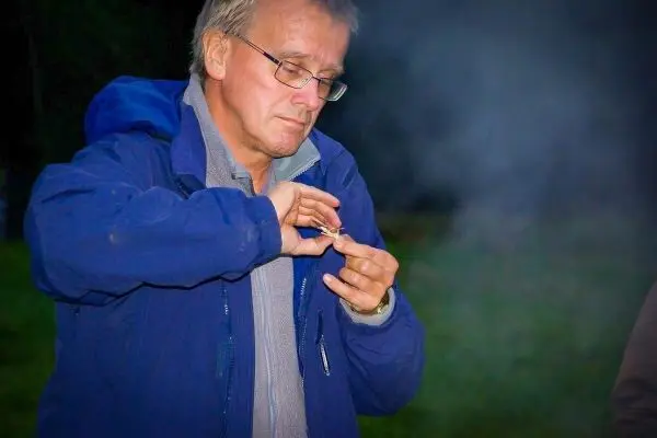 Mann entzündet Zunder mit Feuerstahl in der Hand, Rauch im Hintergrund