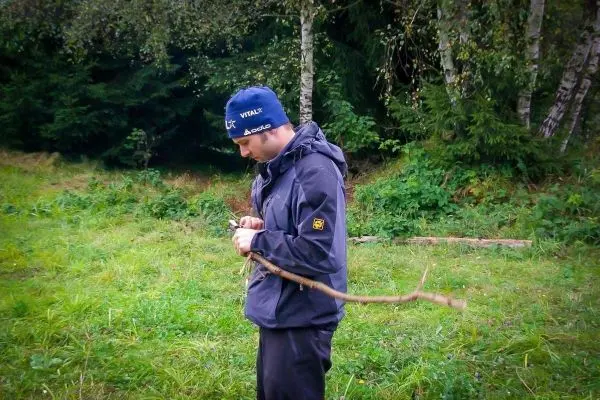 Mann hält einen Stock in der Hand und bearbeitet ihn mit einem Messer