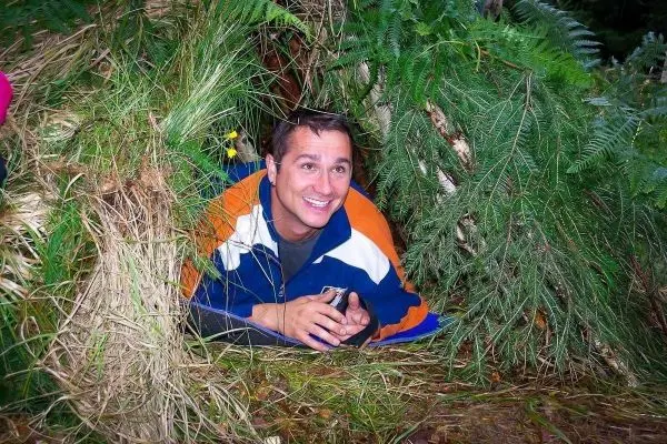 Mann liegt in einer selbstgebauten Unterkunft aus Zweigen und Gras