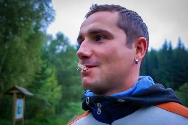 Mann mit Insekt im Mund steht vor Waldlandschaft