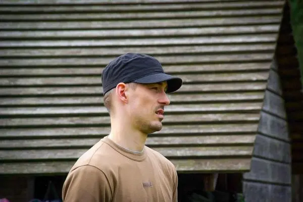 Mann mit Kappe steht vor einer Holzstruktur mit schrägen Dächern