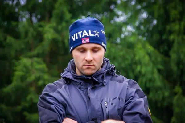 Mann mit Mütze und Jacke steht nachdenklich vor grünen Bäumen