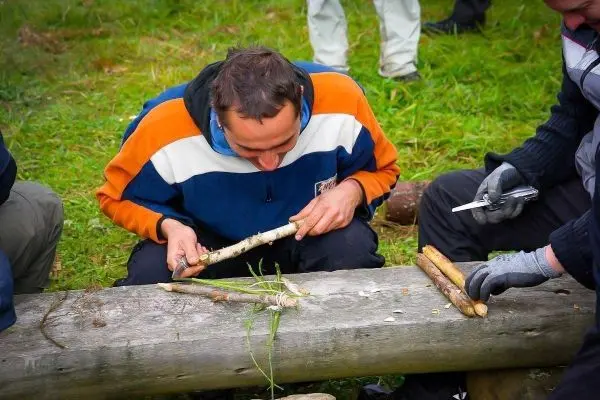 Mann schnitzt mit einem Messer an einem Stock auf einer Holzbank