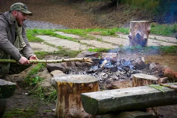Mann stochert mit einem Stock in einem kleinen Bodenfeuer
